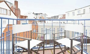 A balcony with a metal railing, two white chairs, and a view of residential buildings. - Holiday Apartment in Norderney With Wi-fi (Norderney)