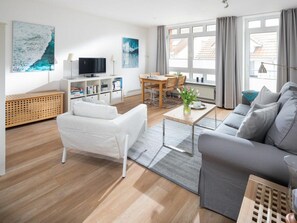 A modern living room with a sofa, a coffee table, and a TV. - Holiday Apartment in Norderney With Wi-fi (Norderney)