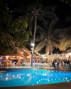 An outdoor pool area with palm trees, a covered seating area, and a bar.
