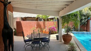 Une terrasse couverte avec une table ronde et des chaises, une plante en pot et une piscine.