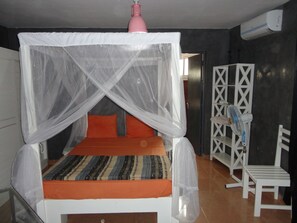 A bed with a mosquito net, an air conditioner, a white chair, and a wardrobe. - Vrbo Property (Saly)