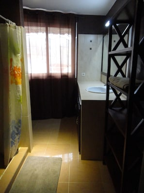 A compact kitchen with a sink, a small countertop, and a window with curtains. - Vrbo Property (Saly)