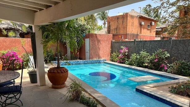 Une piscine avec une terrasse carrelée, une table entourée de chaises et des plantes en pot.