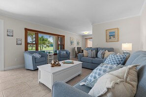 A living room with two sofas, a coffee table, and a lamp. There are two windows with blinds, and a painting on the wall. - 50 Steps to the Beach - 3/2 Island Retreat (Fort Pierce)