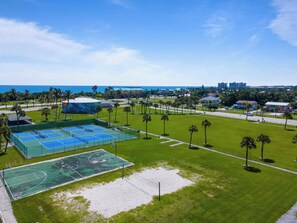 A sports complex with multiple tennis courts, a basketball court, and a sandy area, surrounded by greenery and palm trees. - 50 Steps to the Beach - 3/2 Island Retreat (Fort Pierce)