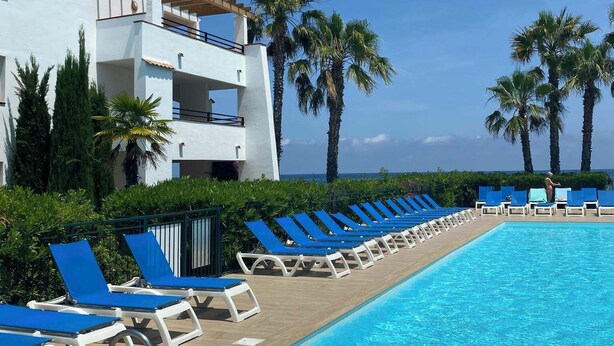 Una piscina con lettini, un edificio con balconi e palme.