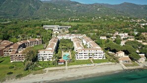 Un hotel sulla costa con diversi edifici, una spiaggia e montagne sullo sfondo.