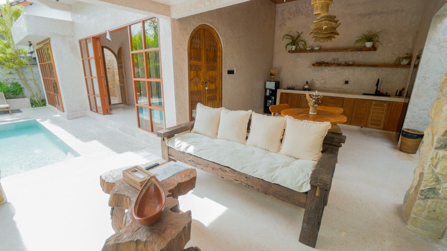 A cozy room with a wooden sofa, a stone table, and a pool in the background.