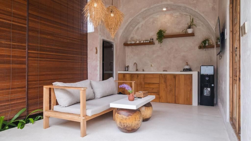 A modern interior with a wooden sofa, a white table, and a kitchen area with wooden cabinets and a refrigerator.