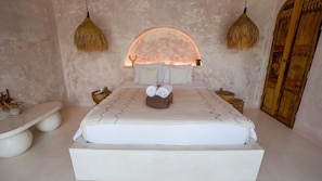 A bedroom with a bed, bedside tables, a wall-mounted lamp, and a wooden door. - Nick Villas (Ubud)