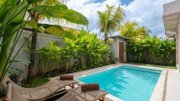 A swimming pool with lounge chairs, surrounded by lush tropical plants.