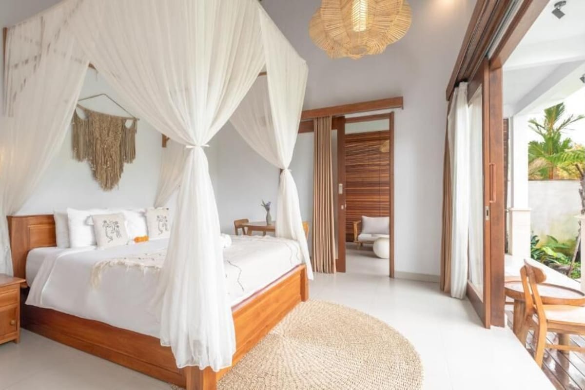 Quarto com cama de dossel, mesa de cabeceira e vista para uma varanda.