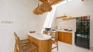A modern kitchen with a central island, wooden chairs, and a hanging light fixture.