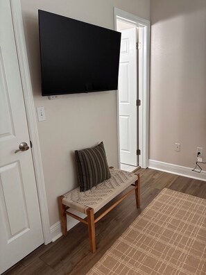 A room with a bench, a flat-screen TV mounted on the wall, and a door. - The Gator’s Den at Lionsgate (Gainesville)