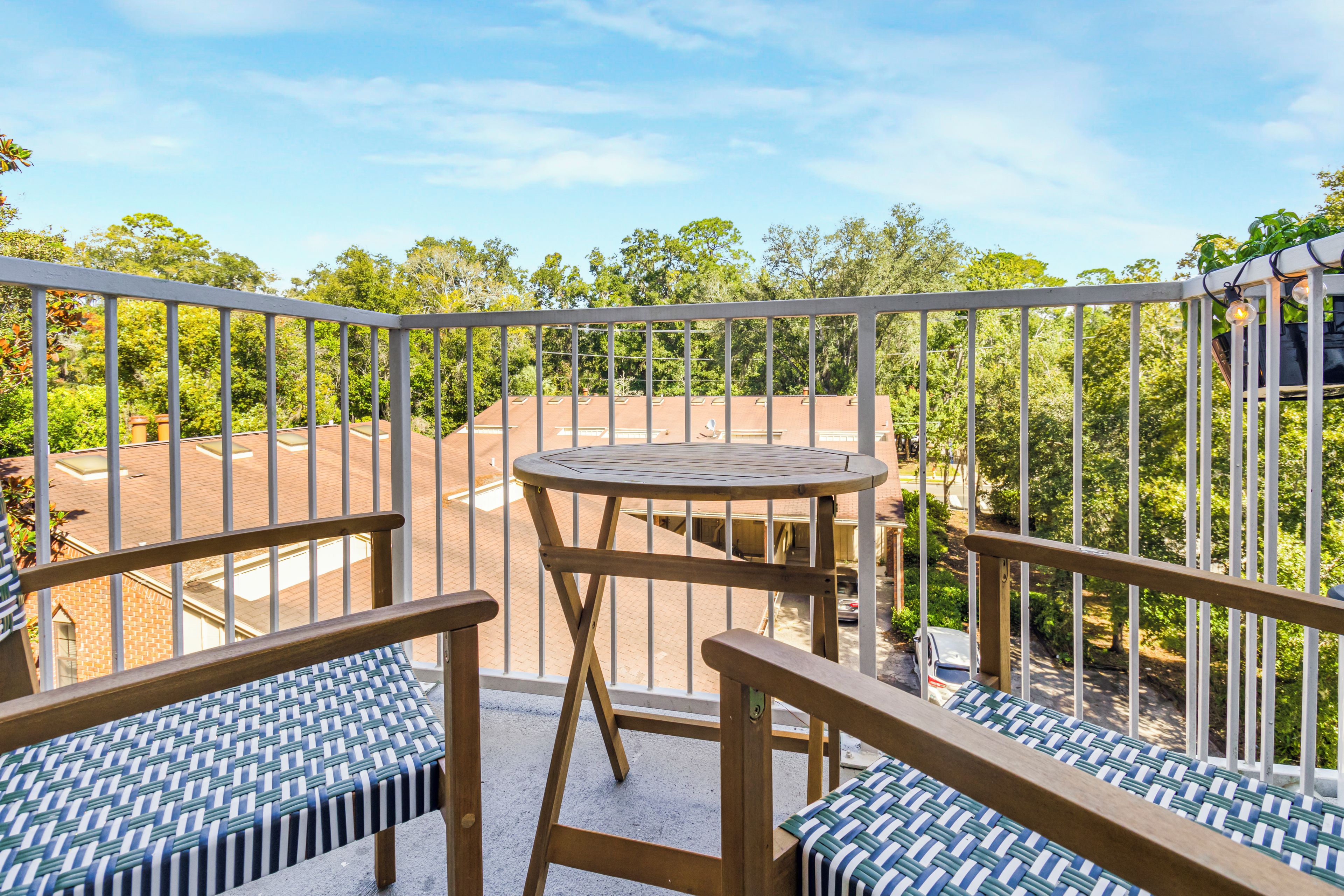 A balcony with a table and two chairs, overlooking a residential area with trees and houses.