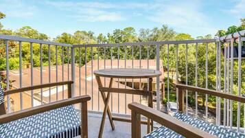 A balcony with a table and two chairs, overlooking a residential area with trees and houses.