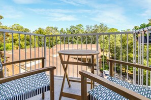 A balcony with a table and two chairs, overlooking a residential area with trees and houses.