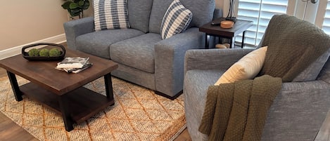 Un salon avec un canapé gris, un fauteuil assorti, une table basse en bois et un tapis à motifs.