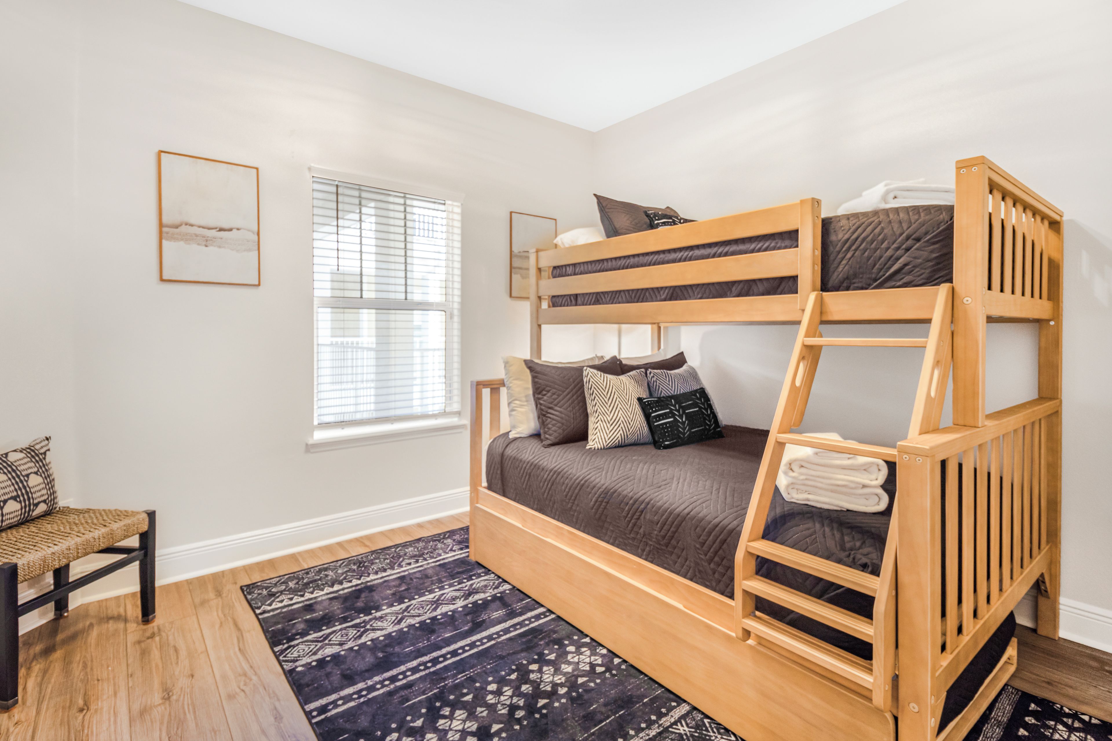 A bunk bed room with a window, a chair, and a patterned rug.