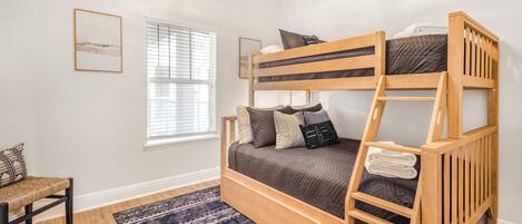 A bunk bed room with a window, a chair, and a patterned rug.