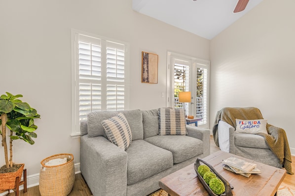 A living room with a grey sofa, a wooden coffee table, and a chair with a Florida license plate pillow.