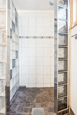 Une salle de bain avec un espace douche, des murs carrelés et un drain.