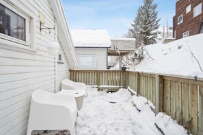 A snow-covered backyard with a wooden fence, a white chair, and a building with a window. - Tromsø apartment - panoramic views and terrace. (Troms)