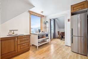 A modern kitchen with wooden cabinets, a stainless steel refrigerator, and a view through the window. - Tromsø apartment - panoramic views and terrace. (Troms)