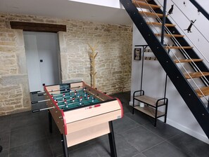 Ein Kicker steht in einem Raum mit Steinwänden, einer Treppe und einem kleinen Regal.