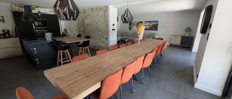 A modern kitchen with a dining area, featuring a long wooden table and orange chairs.