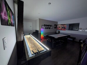 A room with a pool table, a gaming zone sign, and a television.