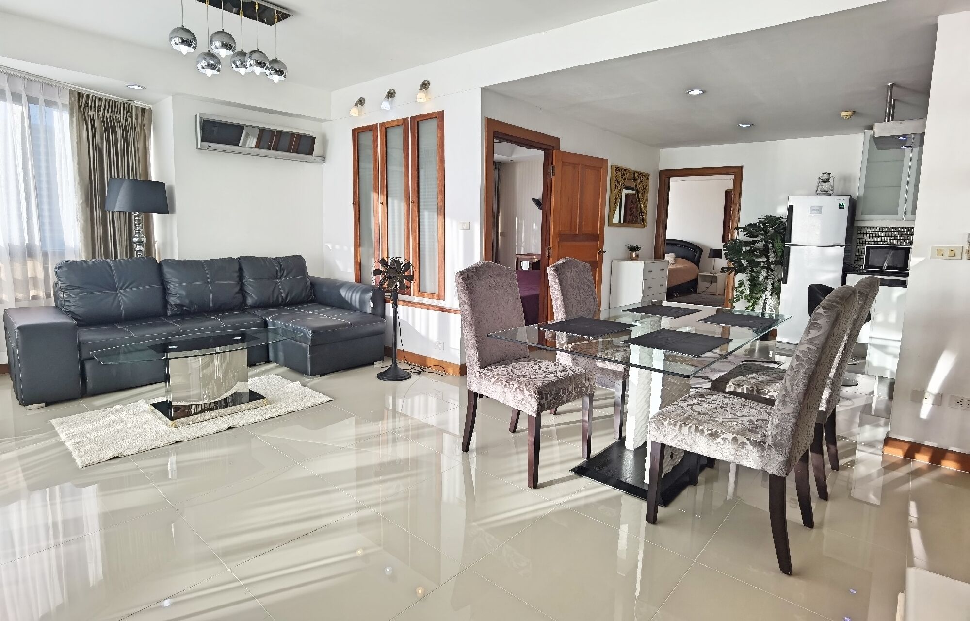 A modern living room with a glass coffee table, a dark leather sofa, and patterned chairs.