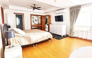 Een slaapkamer met een bed, een dressoir, een televisie en een plafondventilator.