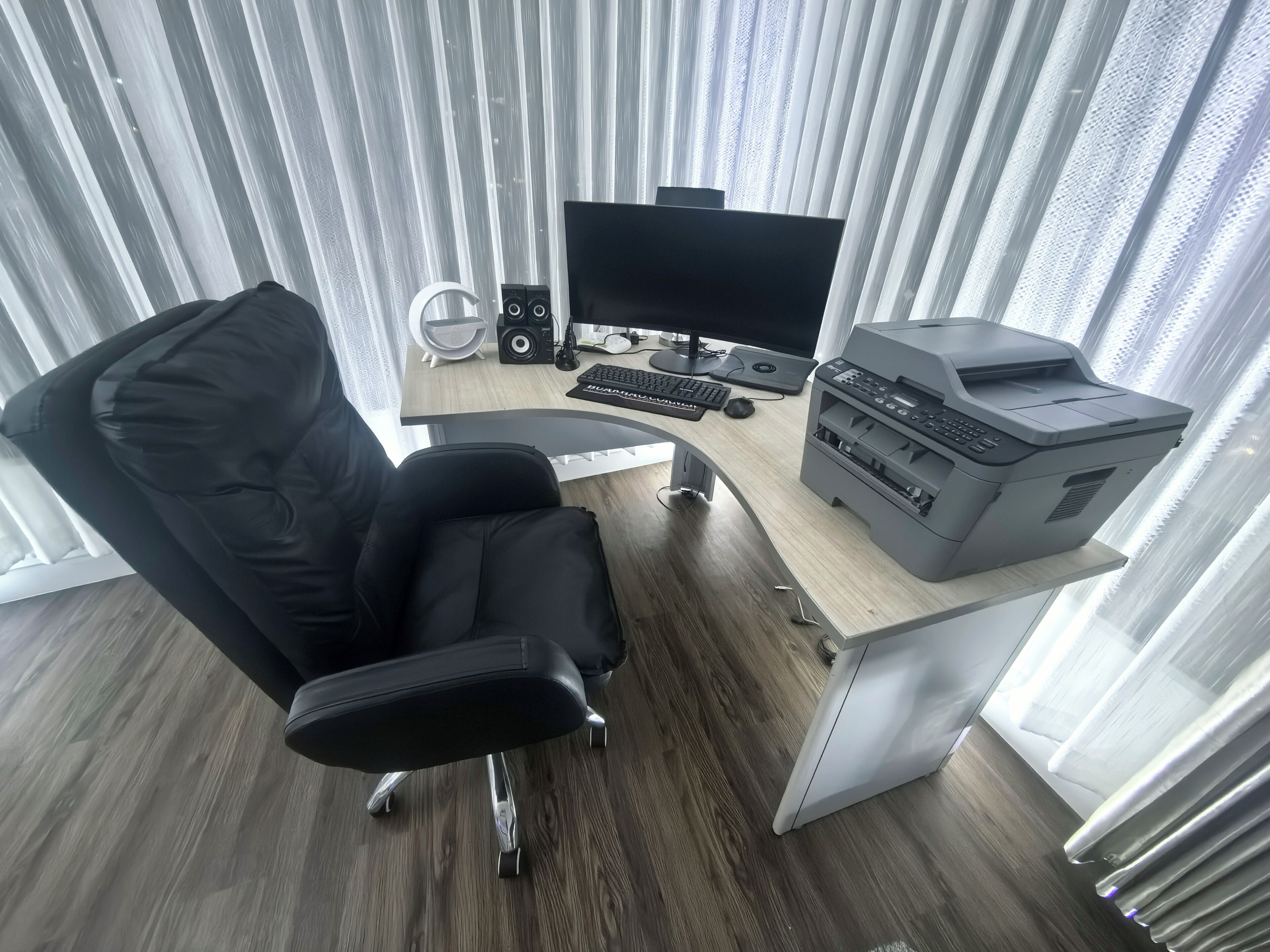A modern office space with a black office chair, a desk with a computer, speakers, and a printer.