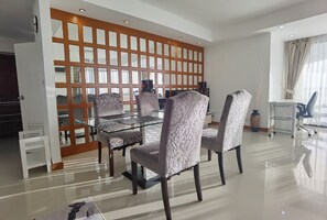 Een moderne eethoek met een glazen tafel en gestreepte stoelen, een decoratieve houten roomdivider en uitzicht op het landschap.