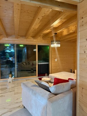 Un interior moderno con techo de madera, un divisor corredero de vidrio que da al exterior, un sofá blanco con cojines y una pequeña mesa redonda con superficie de vidrio.