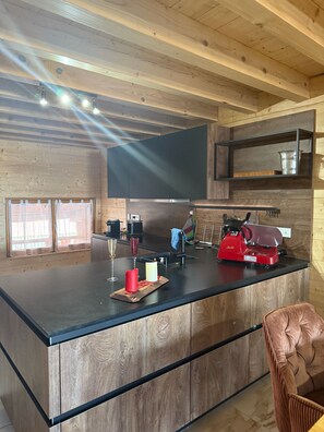 A modern kitchen with a wooden ceiling, a black countertop, and a red espresso machine.