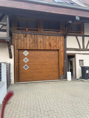 A wooden garage door with diamond-shaped windows, a brick-paved driveway, and a white trash bin.