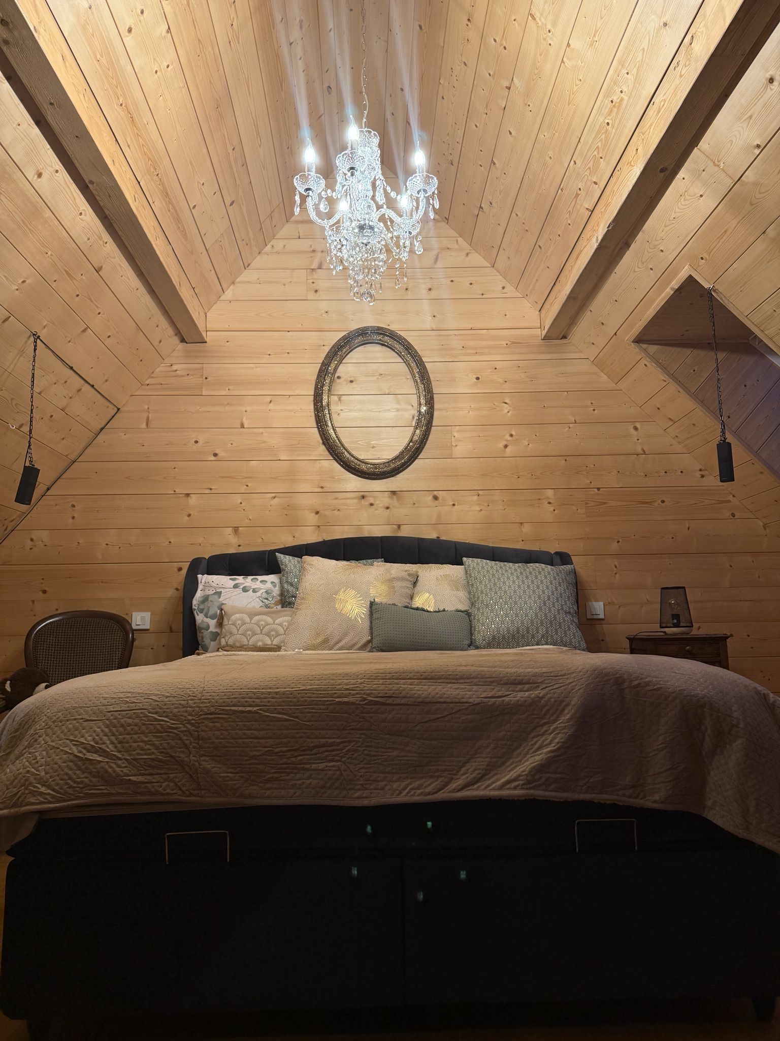 Une pièce aux murs lambrissés, avec un lit, un lustre et un grand miroir rond accroché au mur.