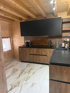A modern kitchen with wooden cabinetry, a black countertop, and a marble floor.