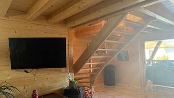 A wooden interior with a TV mounted on the wall, a staircase, and a potted plant.