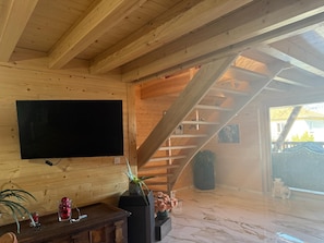 A wooden interior with a TV mounted on the wall, a staircase, and a potted plant.