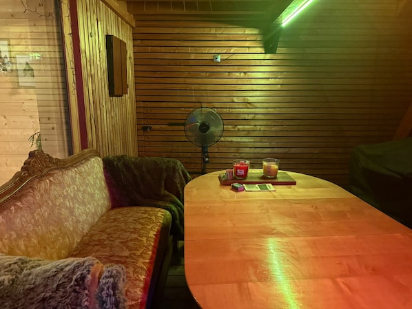 A room with a wooden slatted wall, a sofa, a table with candles, and a fan.