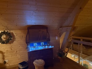 Un interior de madera con chimenea, un adorno de guirnalda y un pequeño cubo de basura.