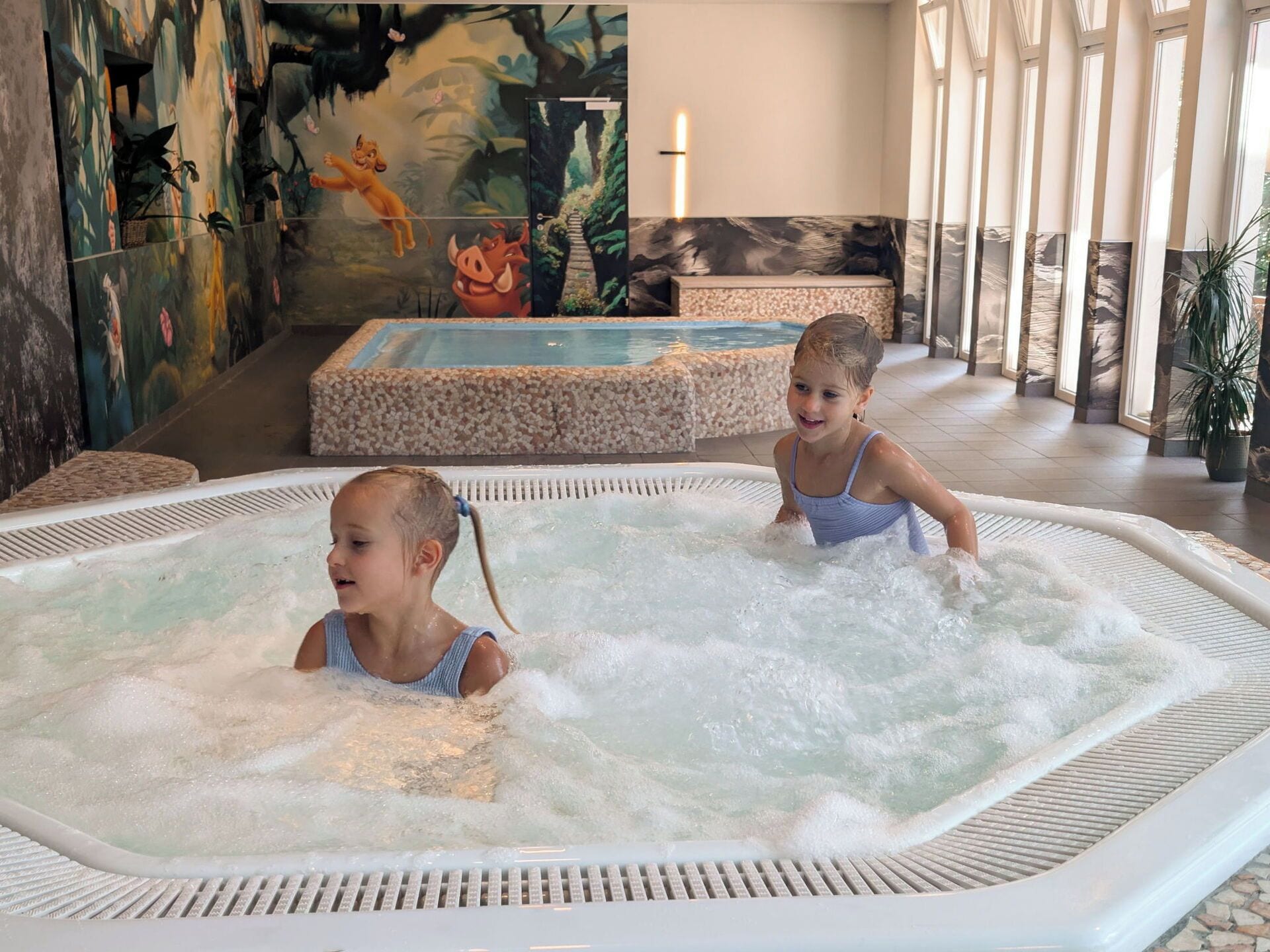 A hot tub area with a mural, a seating area, and a view of the outdoors.