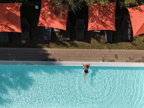 Une piscine à l’eau claire, entourée d’un mur de briques et de parasols rouges.