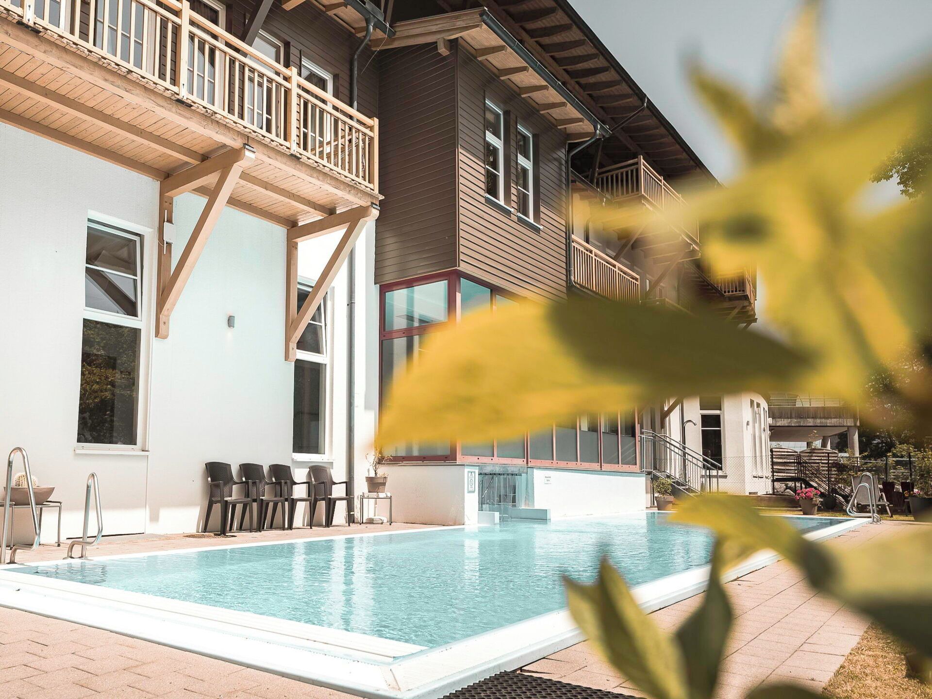 A swimming pool with a wooden deck, outdoor seating, and a building with a balcony.