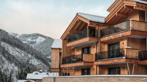 Ein mehrstöckiges Holzhaus mit Balkonen vor einer verschneiten Berglandschaft.