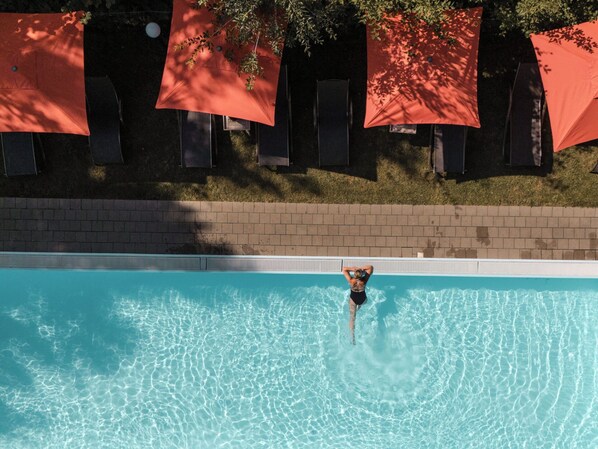 Ein Schwimmbecken mit klarem Wasser, umgeben von einer Ziegelmauer und roten Sonnenschirmen.