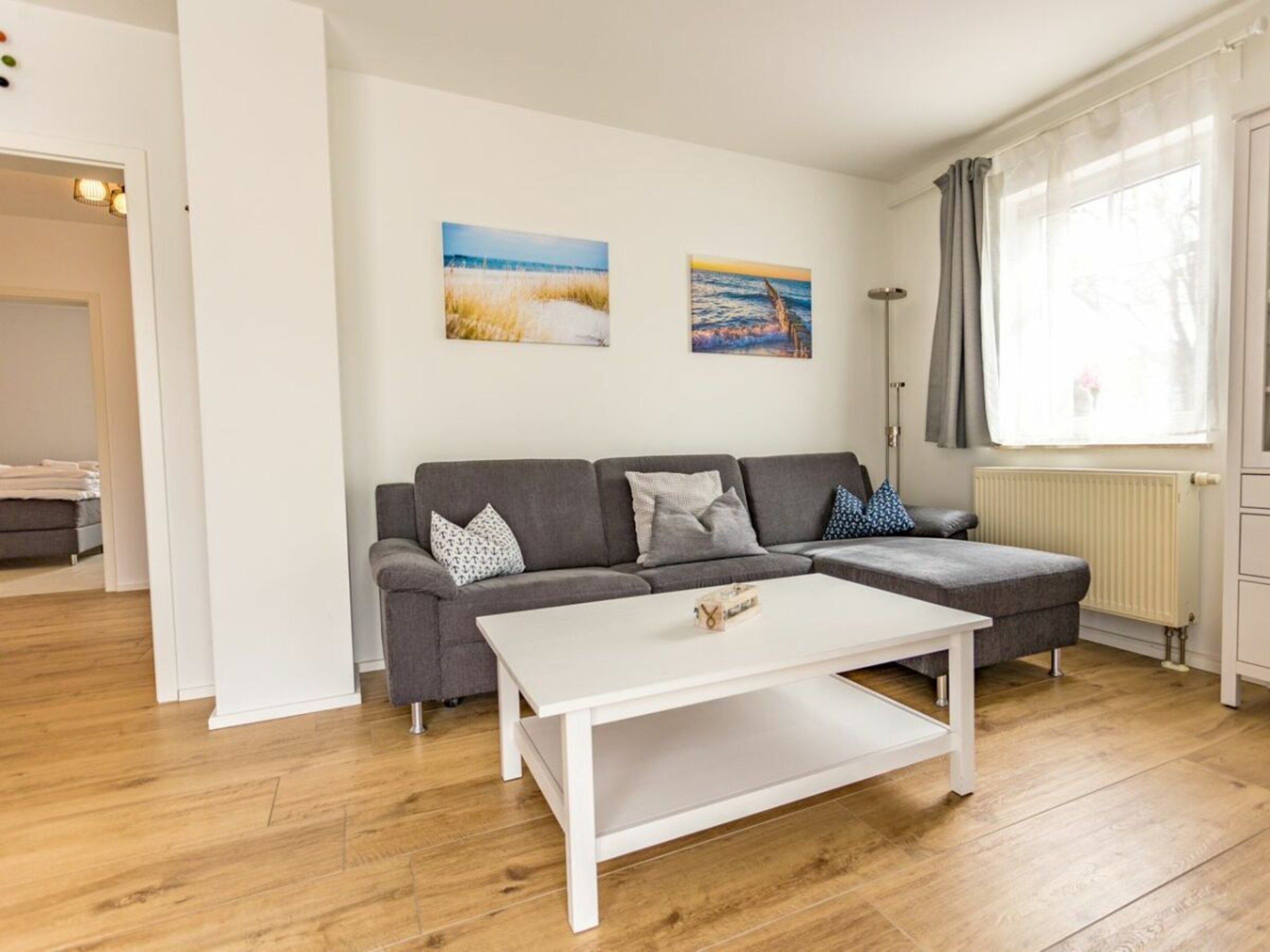 A living room with a grey sectional sofa, a white coffee table, and two wall-mounted paintings.